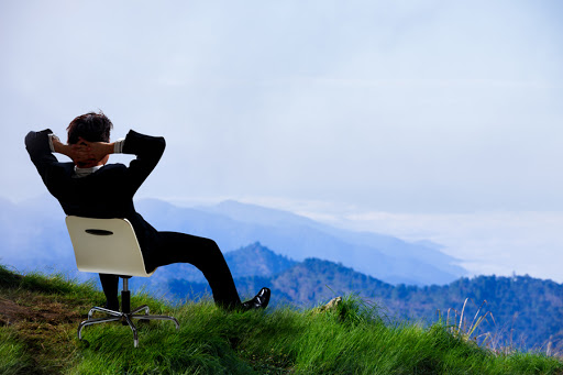 Young businessman who sits on a chair at the top of the mountain and looks into the sky &#8211; pt