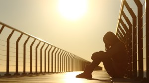 Sad teenager girl depressed sitting in the floor of a bridge on the beach at sunset