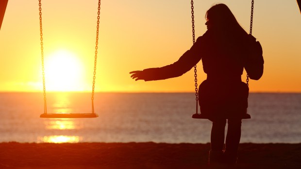 Single or divorced woman alone missing a boyfriend while swinging on the beach at sunset