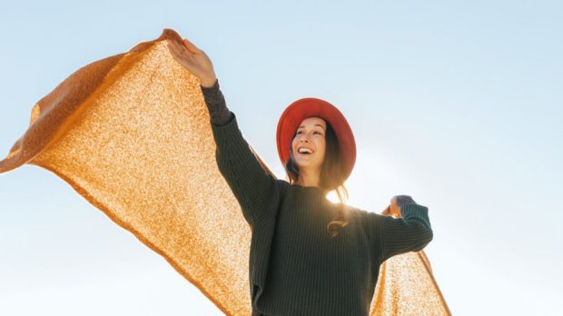 Joyful teen woman playing with a blanket over a clear sky