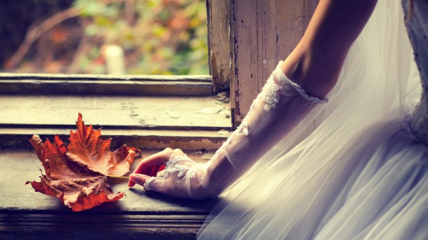 Detail of the brides hand holding autumn leaf while sitting in front of the window.