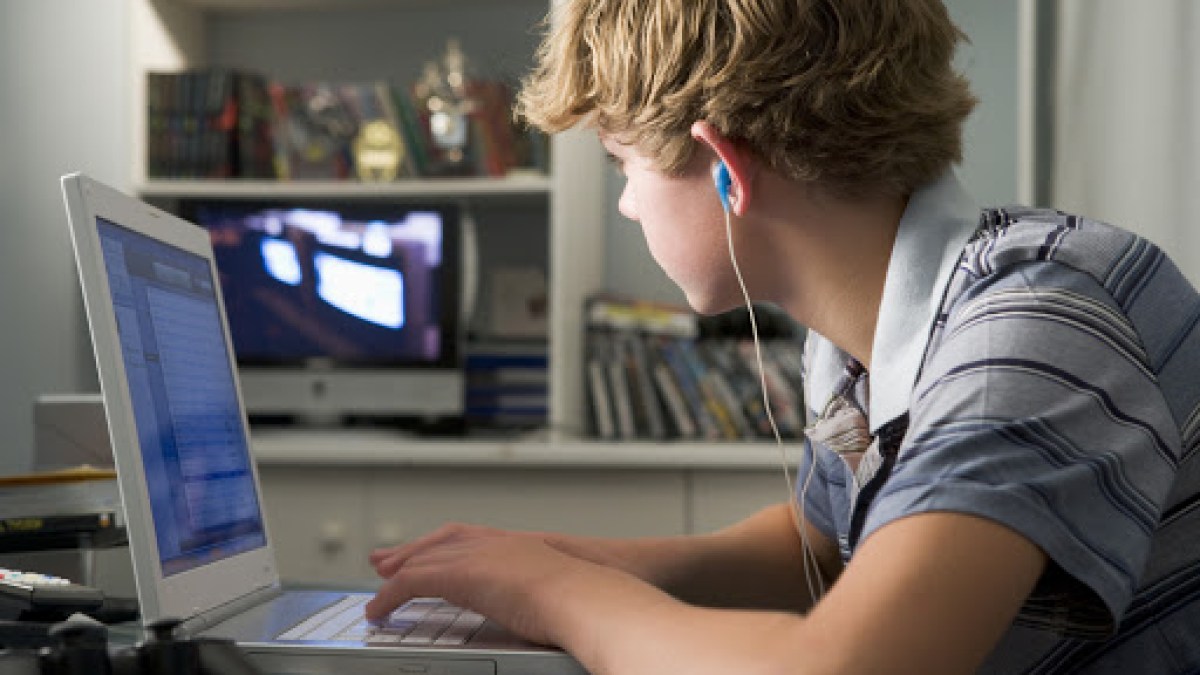 Young boy in bedroom using laptop and listening to MP3 player – es