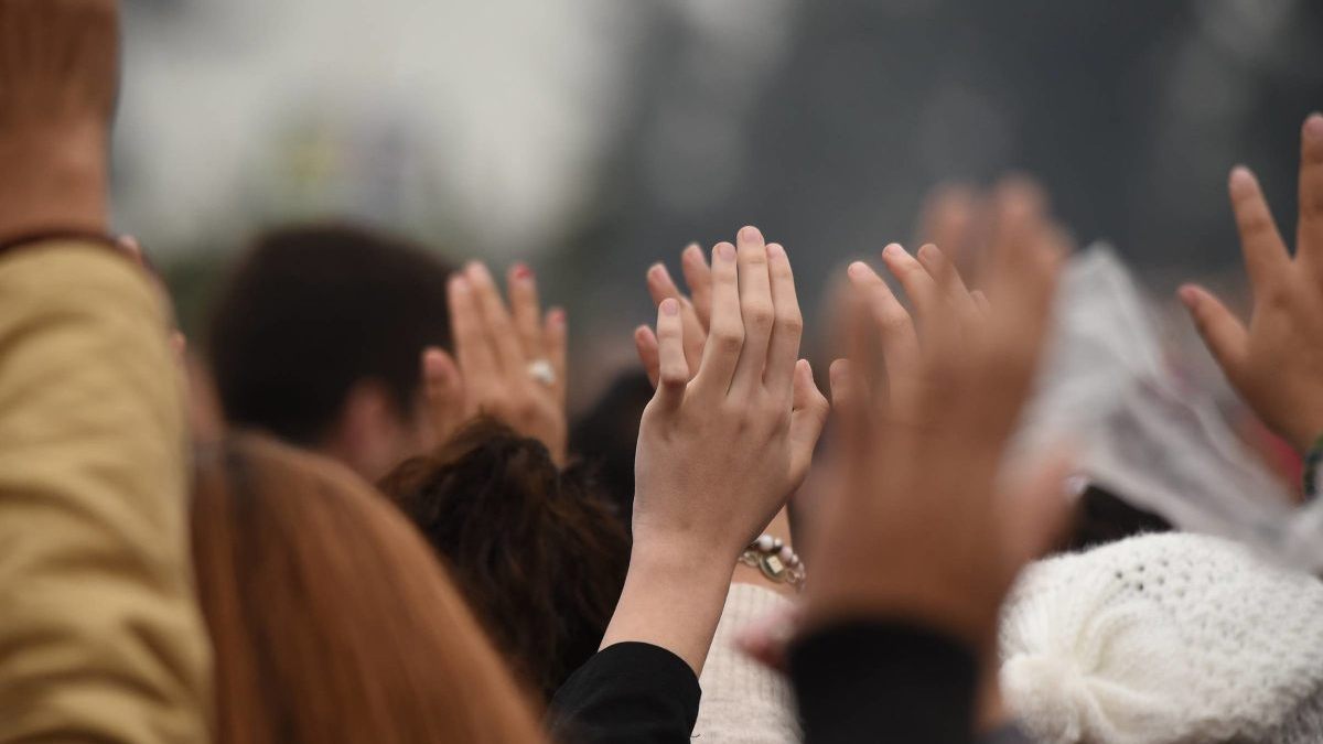 PESSOAS NA MISSA COM MÃOS ERGUIDAS