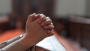 Mãos de mulher rezando em igreja