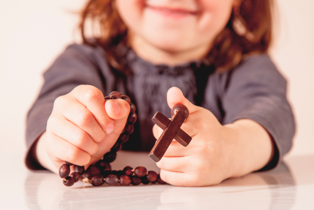 Little girl holds rosary and smiles