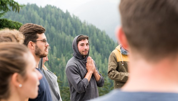 young group of men and women stand in a circle and prepare to have a group prayer outdoors