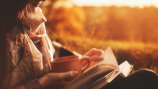 woman sits near a tree in an autumn forest and holds a book