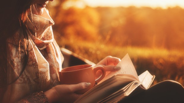 woman sits near a tree in an autumn forest and holds a book