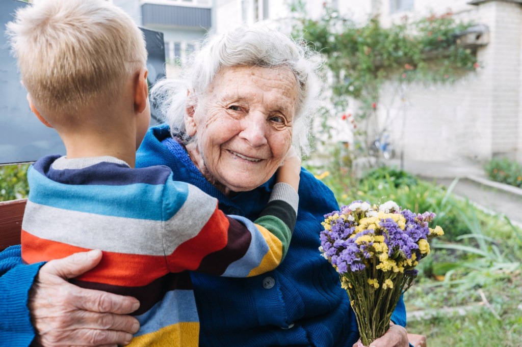 Wnuczek przytula babcię po tym, jak wręczył jej w prezencie bukiet kwiatów