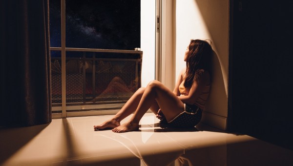 Sad woman sitting on floor looking out window