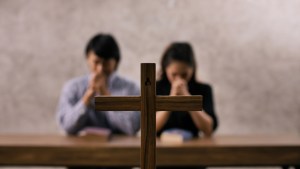 Casal rezando em frente a cruz