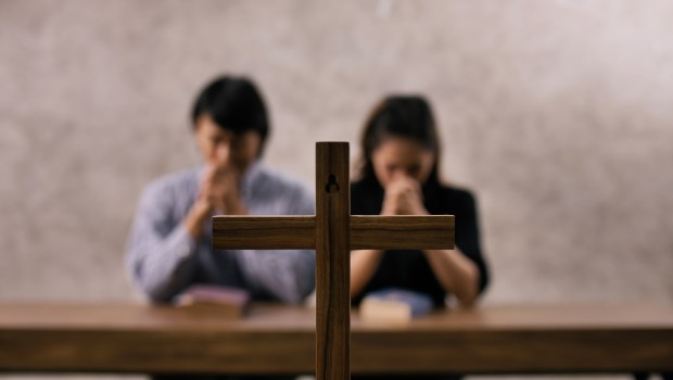 Casal rezando em frente a cruz