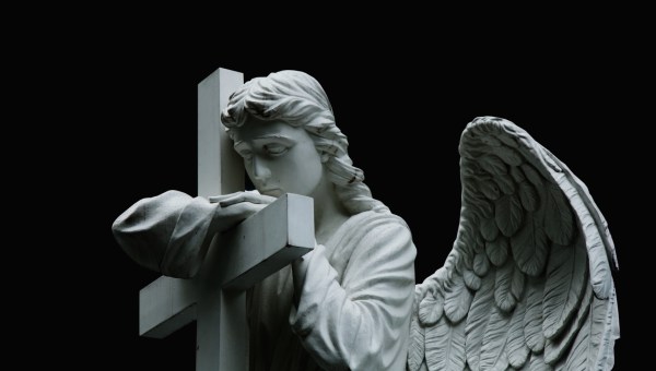 Smutny kamienny anioł stoi z krzyżem