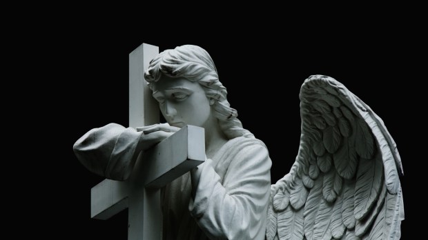 Smutny kamienny anioł stoi z krzyżem