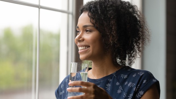 Mulher com copo de água na mão e sorrindo na janela