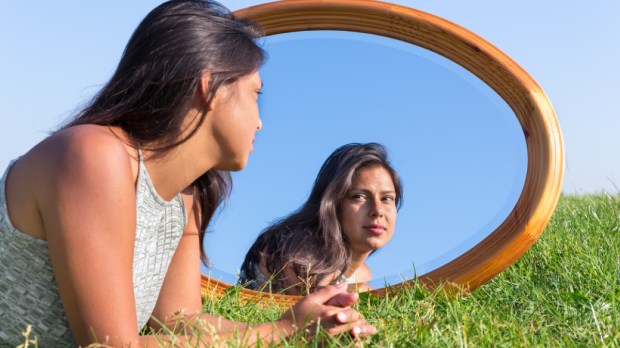 Woman lying on grass looking at her mirror image