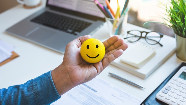 Mão segurando bolinha de emoji feliz