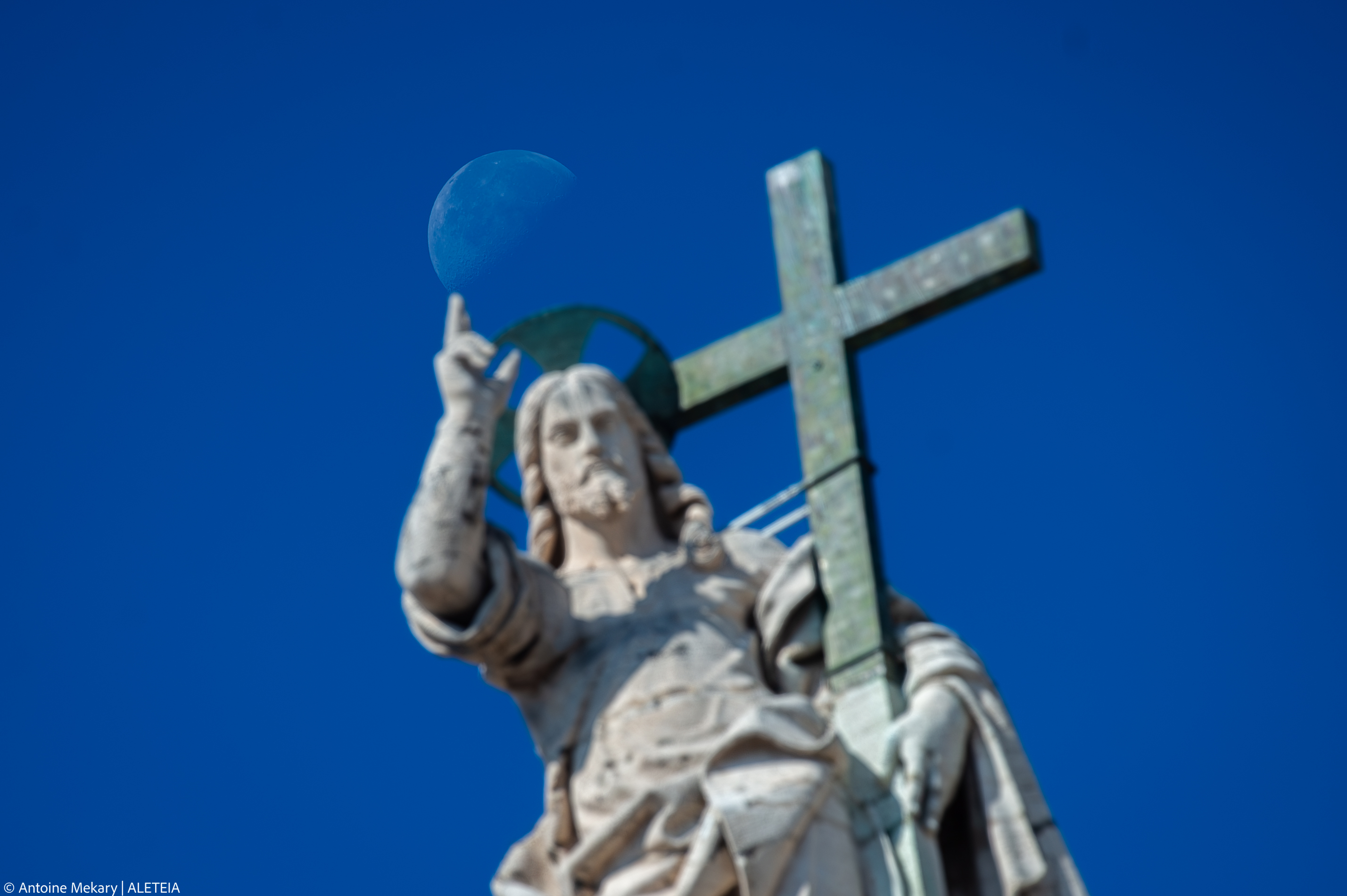 A moon rises over a statue of Jesus Christ