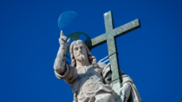 A moon rises over a statue of Jesus Christ