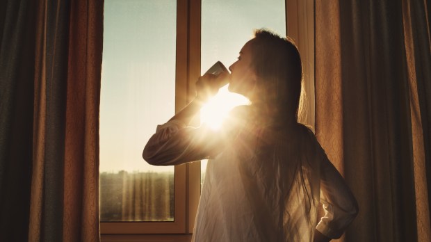Kobieta pije kawę stojąc w oknie wczesnym rankiem