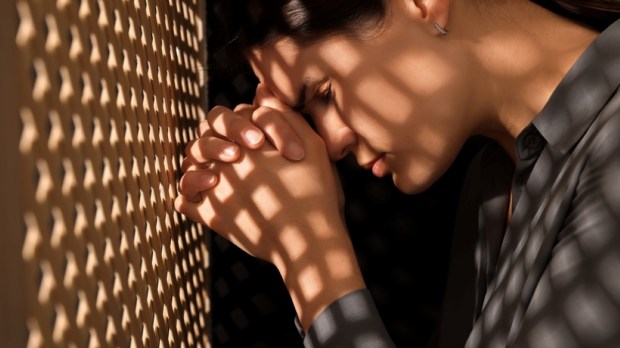 Repentant woman during confession near wooden partition in booth