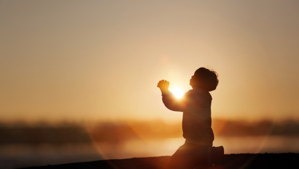 Dziecko modli się na tle słońca