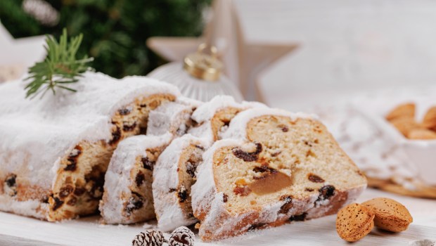 Christmas stollen loaf with a sugar coating, sliced and displayed with almonds, pinecones, and festive ornaments, capturing the spirit of the holiday season.